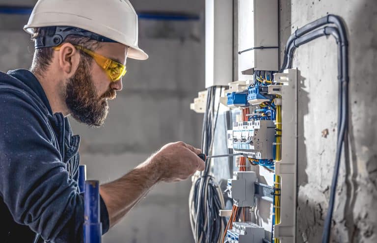 A male electrician works in a switchboard with an electrical connecting cable.